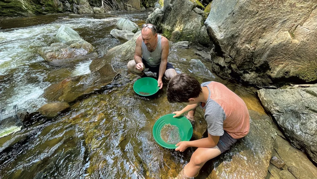 Ein Vater und sein Sohn waschen Gold in einem schnell fließenden Fluss mit grünen Waschpfannen.