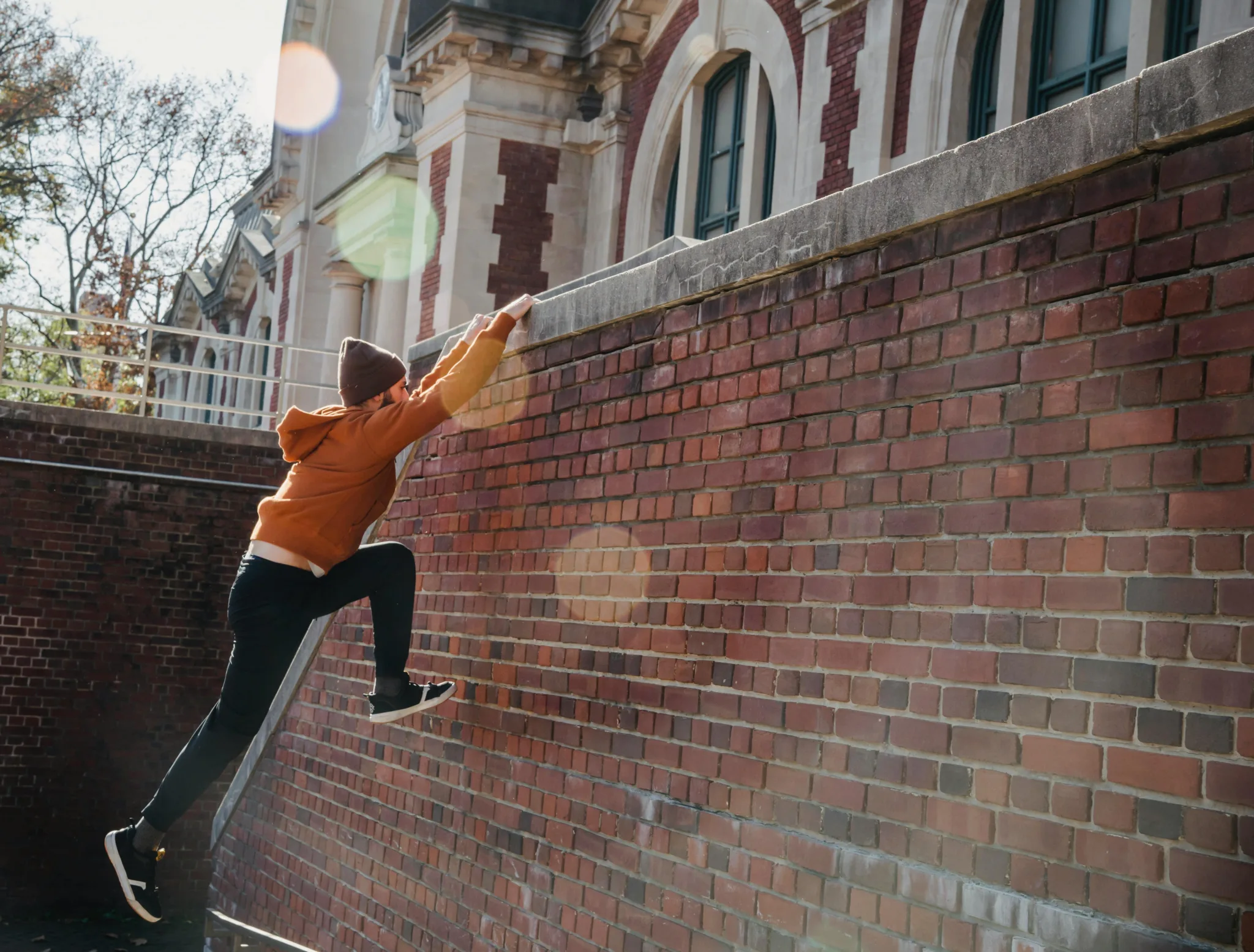 Ein Parkourläufer in einer gelben Jacke springt auf eine Ziegelmauer.